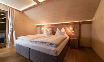 A cozy bedroom with a double bed and artistic pillows. The walls are made of wood and the lighting is soft and inviting.