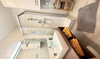 A modern bathroom with a shower, sink, and mirror.  
Towels are neatly stacked on a shelf.