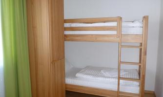 A simple room with a wooden bunk bed. The room has a wardrobe and a window with green curtains.