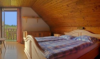 A cozy bedroom with wooden walls and a large window. The room features a double bed and a small seating area.