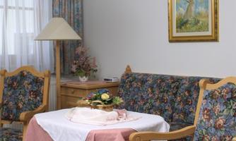 A cozy living space with a table surrounded by floral-decorated chairs. A small picture hangs on the wall, and the room is bright and inviting.