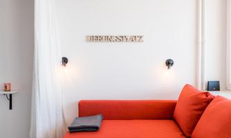 A modern living room with a red sofa and soft lights. On the wall hangs a sign that reads "DEUTSCHPLATZ".