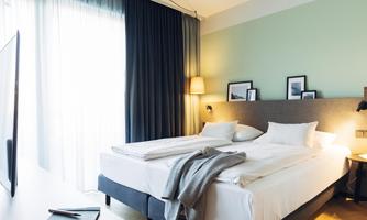 A modern bedroom with a large bed and soft colors. The windows let in plenty of daylight, creating a cozy atmosphere.