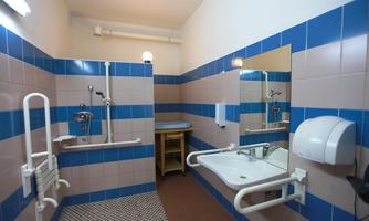 A modern bathroom with blue and white tiles. There is a shower, sink, and grab bars for accessible design.