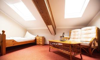 A cozy attic room with a wooden bed and a rattan sofa. Large windows provide plenty of light in the room.