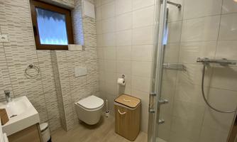 A modern bathroom with a shower, sink, and toilet. The walls are equipped with light tiles and a window.