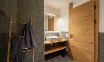 A modern bathroom with gray walls and wooden details. There is a sink, a mirror, and a towel rack.
