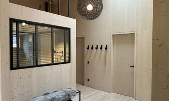 A modernly designed entrance area with bright wooden walls. On the wall, there are coat hooks and a comfortable seating furniture.
