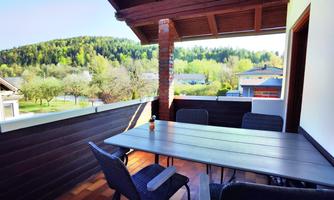 A cozy balcony with a table and chairs. In the background, green hills and trees can be seen.