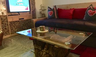 A cozy living space with a sofa, red cushions, and a coffee table made of a tree trunk. On the wall, there is a television and wooden decor for a warm atmosphere.