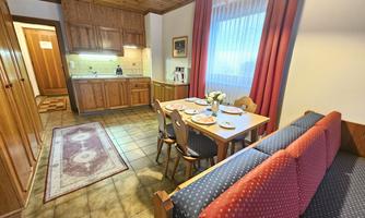 A cozy kitchen with a dining table and wooden shelves. The room has bright walls and a large window overlooking nature.
