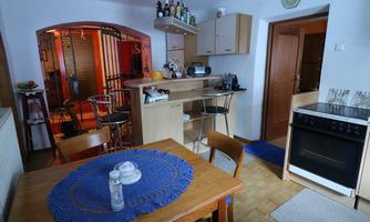 A cozy kitchen with a table and chairs. In the background, a cooking area and a bar with several drinks are visible.