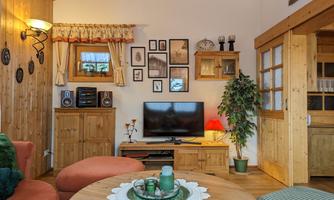 A cozy living room with wooden shelves and a television. The walls are decorated and there is a green plant in the corner.