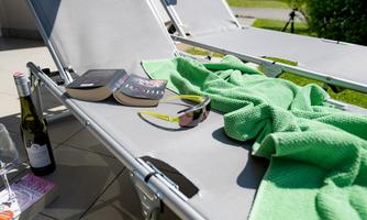 A cozy lounge chair with a green towel, a book, and sunglasses. Next to the chair is a bottle of champagne.