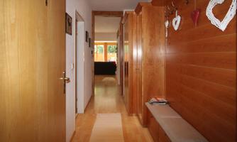 A cozy hallway with wooden paneling and a bench. Decorative hearts are hanging on the wall, and there is plenty of daylight visible.