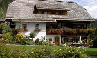 A traditional old house with a sloped roof and a colorful flower garden. Surrounded by green mountains, it offers a picturesque and inviting atmosphere.