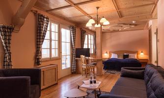 A cozy room with wooden furniture and large windows. There is a double bed, a television, and a seating area with a table.