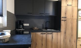 A modern kitchen with wooden and dark surfaces. The equipment includes a faucet, a coffee machine, and a sink.