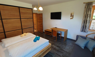 A modern room with two beds, a table, and a sofa. The wall is clad with wooden panels and there is a television.