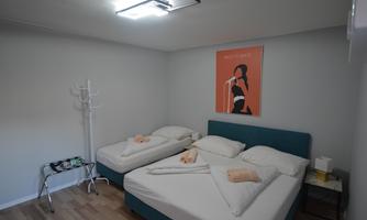 A simple bedroom with two single beds and a modern poster on the wall. The walls are light and the floor is wooden.