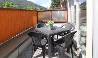 A balcony with a black table and four chairs. On the table, there is a flower pot, and in the background, mountains can be seen.