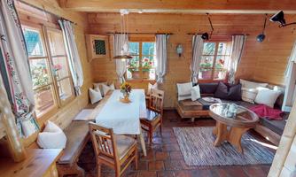 A cozy wooden house with a dining table and a seating area. Large windows let in plenty of light and offer a view of the flowers outside.