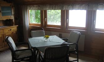 A cozy dining area with a table and four chairs. Large windows let in plenty of light and offer a view of the outdoors.