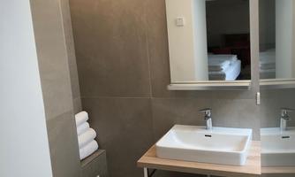 A modern bathroom with a sink on a wooden shelf. There are towels, a mirror, and a clean, bright atmosphere.