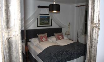 A cozy bedroom with a large bed and decorative pillows. It features an impressive mirror as well as soft lighting.