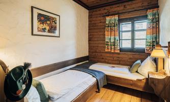 A cozy room with wooden paneling and two beds. Colorful curtains and a window create an inviting atmosphere.