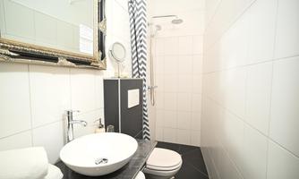 A modern bathroom with a shower, a large mirror, and an elegant sink. The walls are in neutral colors, and there are fresh towels.