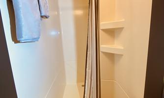 A simple shower room with light walls and a shower curtain. Towels and a rug are ready.