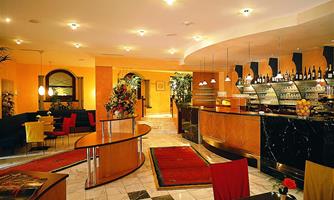 An elegant lobby with a modern reception desk and stylish furnishings. The walls are painted in warm colors, and there are plants as well as cozy seating areas.
