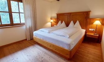 A cozy bedroom with a double bed and wooden details. Bright windows create a friendly atmosphere.