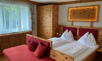 A cozy bedroom with paneling and a double bed. The room is bright and friendly, with a red sofa and large windows.