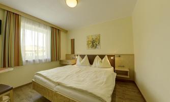 A modern hotel room with a large double bed and hardwood floor. It has large windows that let in plenty of natural light and a subtle color selection.