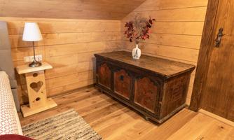 A cozy room with wood paneling and an antique chest furniture. On the table, there is a lamp and a vase with decoration.