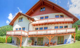 A modern holiday home with multiple balconies and spacious windows. The surroundings are green and inviting, ideal for relaxing stays.