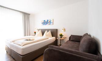 A bright and modern room with a double bed and a gray sofa. The decor is simple and inviting, perfect for relaxing.