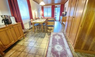 A cozy living space with wooden paneling and a dining area. The room is friendly and bright, with windows that lead to a balcony.