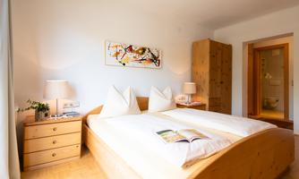 A cozy bedroom with a wooden double bed and two nightstands. The walls are light, and there are artworks as well as pleasant lighting.