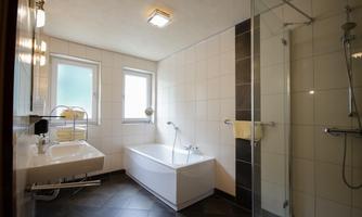 A modern bathroom with a bathtub and a shower. It features bright walls and large windows that let in plenty of light.