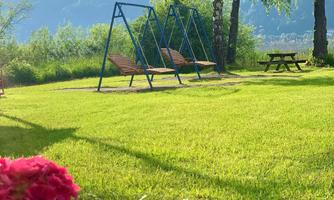 A peaceful garden with a swinging playground and beautiful green grass. In the foreground, pink flowers are blooming.