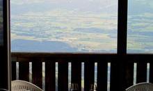 A view from a balcony with white chairs and a small table. In the background, a wide landscape with gentle hills can be seen.