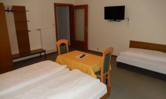 A simple room with two beds, a table and chairs. A television and a wardrobe are also available.