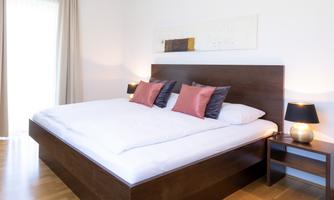 A modern bedroom with a large double bed and stylish pillows. The warm wood tones and soft lighting create an inviting atmosphere.