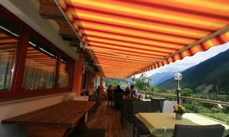A cozy balcony with striped awnings in orange and yellow. In the background are mountainscapes and guests relaxing.