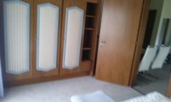 A room with a large wooden cabinet and an open shelf. In the background, modern chairs are visible.