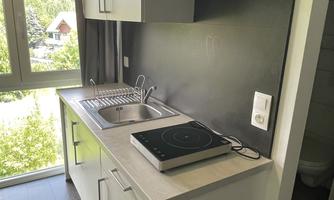A modern kitchen with white cabinets and an electric stove. The room has large windows that let in plenty of daylight.