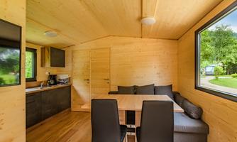 A modern wooden house with a cozy dining area. Large windows offer a view of the greenery.